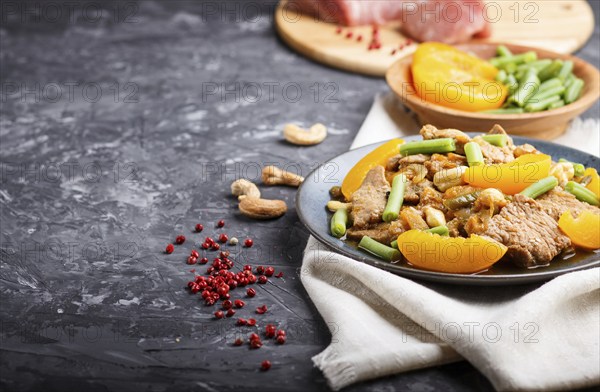 Fried pork with peaches, cashew and green beans on a black concrete background. side view, copy space, selective focus, chinese cuisine. linen textile