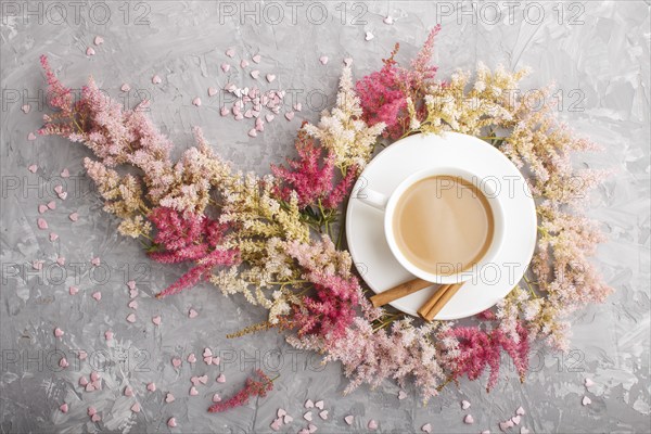 Pink and red astilbe flowers and a cup of coffee on a gray concrete background. Morninig, spring, fashion composition. Flat lay, top view