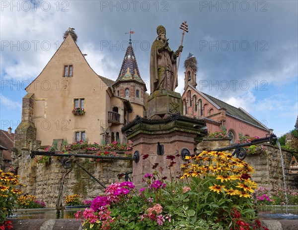 The St. Leon fountain on Saint-Leon Square in the centre of Eguisheim in Alsace. Well-kept half-timbered houses and floral decorations characterise the town centre. The town is classified as one of the Plus beaux villages de France. Eguisheim, Haut-Rhin, France, Europe