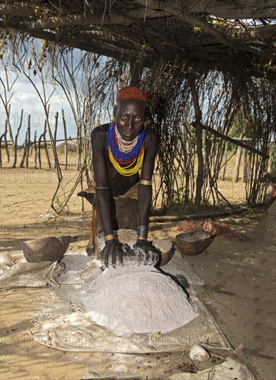 Woman from the Arbore ethnic group grinding red sorghum millet on a grinding stone, Southern Omo Valley, Ethiopia, Africa