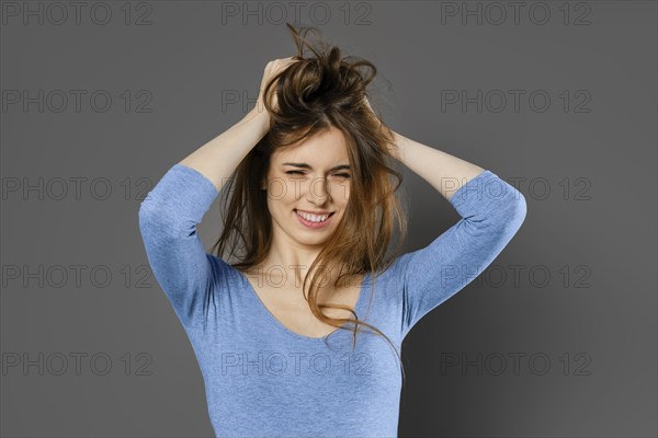 Young woman fooling around and mussing her hair with her hands over grey studio background