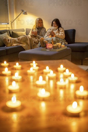 Symbolic image energy saving, cold winter, energy crisis, cold flat, mother and daughter lying on the sofa, warmly dressed, candlelight, heating on to a minimum