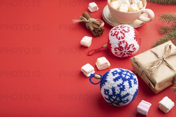 Christmas or New Year composition. Decorations, box, cinnamon, knitted balls, fir and spruce branches, cup of coffee, on a red paper background. Side view, copy space