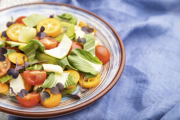 Vegetarian salad of pac choi cabbage, kiwi, tomatoes, kumquat, microgreen sprouts on a white concrete background and blue linen textile. Side view, close up, selective focus