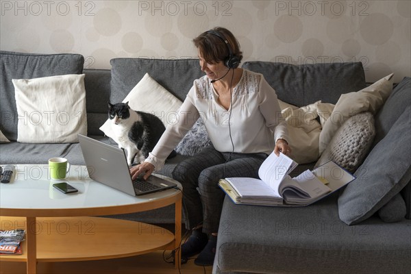 Woman, mid-50s, works from home, with laptop and communicates with colleagues via headset, home office, on the sofa