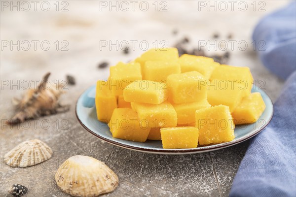 Dried and candied mango cubes on blue plate on brown concrete background and linen textile. Side view, close up, selective focus, vegan, vegetarian food concept