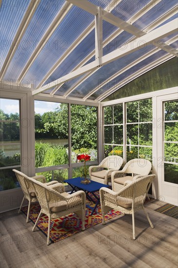 Beige wicker armchairs and blue wooden table in sunroom at back of luxurious residential home, Quebec, Canada, North America