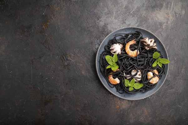 Black cuttlefish ink pasta with shrimps or prawns and small octopuses on black concrete background. Top view, flat lay, copy space