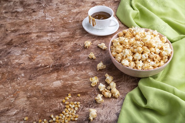 Popcorn with caramel in ceramic bowl on brown concrete background and green textile. Side view, copy space