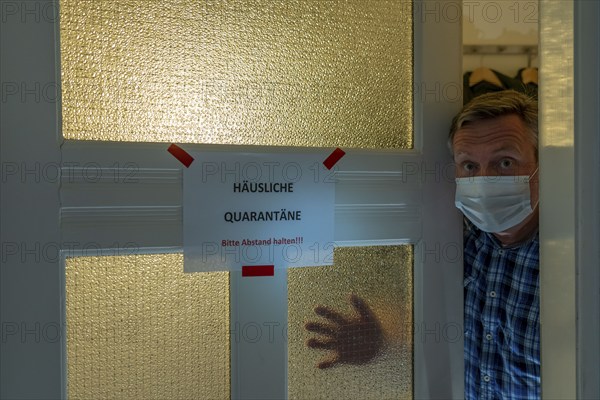 Symbolic image Domestic quarantine, man is in isolation at home due to a suspected corona infection, warning sign for visitors on the front door, communicating with a visitor through the door