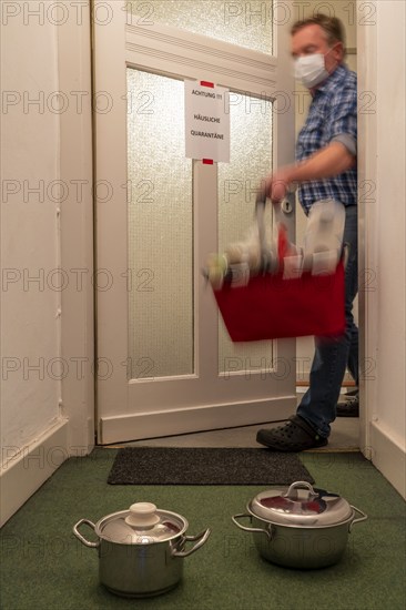 Symbolic image Domestic quarantine, man is in isolation at home due to a suspected corona infection, warning sign for visitors on the front door, communicates with a visitor through the door, neighbours have been shopping, cooked and put the things in front of the door