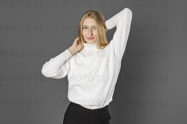 Cheerful woman holding her hands behind her head on grey background