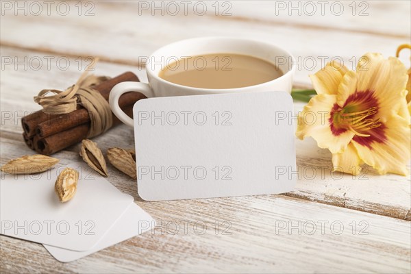 White paper business card mockup with orange day-lily flower and cup of coffee on white wooden background. Blank, side view, copy space, still life. spring concept