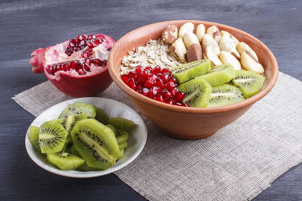 A plate with muesli, kiwi, pomegranate, Brazil nuts on a black wooden background. close up