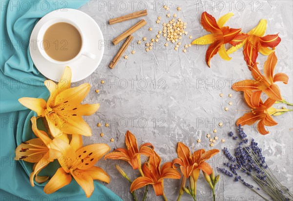 Orange day-lily and lavender flowers and a cup of coffee on a gray concrete background, with blue textile. Morninig, spring, fashion composition. Flat lay, top view, copy space