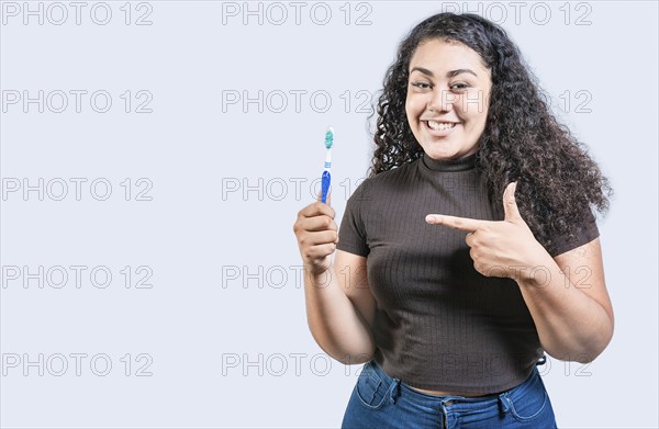 Smiling woman holding and pointing a toothbrush. Happy girl holding and pointing at toothbrush isolated