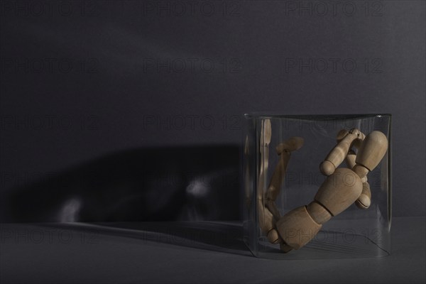 Wooden mannequin locked in a glass cube on gray background. captivity, break rules, loneliness, depression disorder concept. copy space