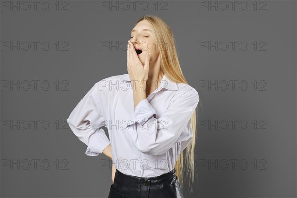 Young woman yawns covering her mouth with her hand