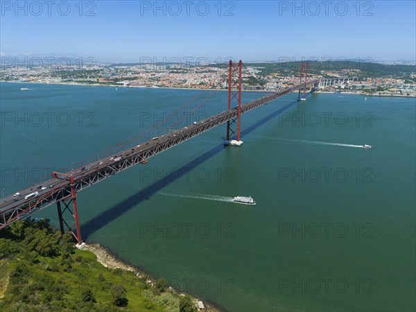 Red bridge spanning the water, lined with boats, with a city and nature in the background on a sunny day, aerial view, Ponte 25 de Abril, bridge of 25 April, suspension bridge over the Tagus, double deck bridge, road traffic and railway traffic, Lisbon, Lisboa, Portugal, Europe