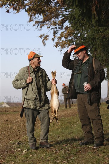 Hunter with hunted hare (Lepus europaeus) receives a hunter's greeting from a hunting companion, Lower Austria, Austria, Europe