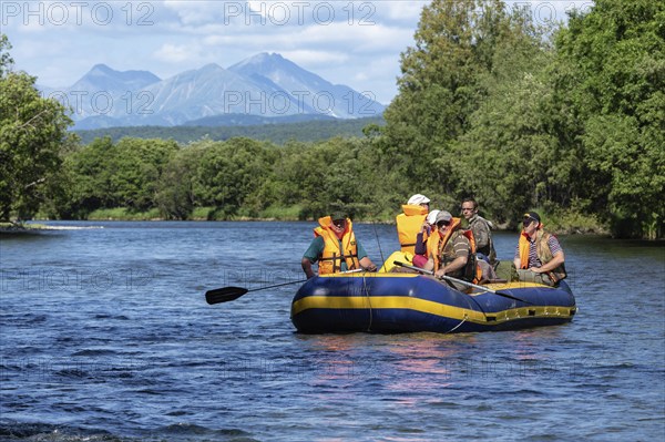 FAST RIVER, KAMCHATKA PENINSULA, RUSSIAN FAR EAST, JULY 25, 2016: Summer rafting on Kamchatka, group of tourists, travelers floating on calm river on raft on background of mountains and green forest