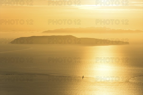 Small island and lonely sailing boat on the ocean during dramatic golden sunset