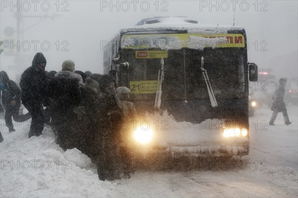 PETROPAVLOVSK CITY, KAMCHATKA PENINSULA, RUSSIA, DECEMBER 26, 2017: Winter city life during heavy snow winter storm, passengers boarding at bus stop on public transport, commercial city bus