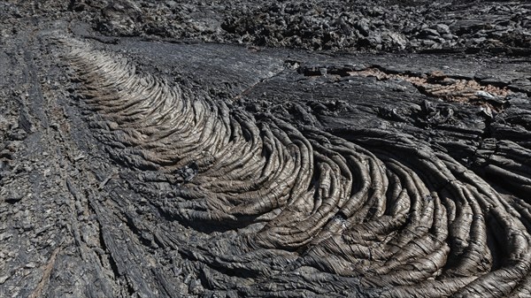 Lava field volcano landscape of Kamchatka Peninsula: view of smooth, undulating surface of black frozen lava flow, which wrinkled in tapestry-like folds and rolls resembling twisted. Active Plosky (Flat) Tolbachik Volcano in Russian Far East