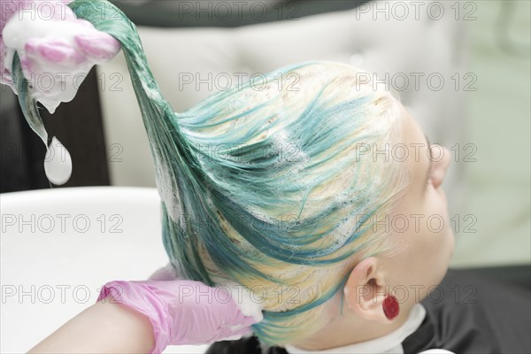 Washing green hair color of young woman with shampoo in sink. Working hairdresser in pink protective gloves in beauty salon