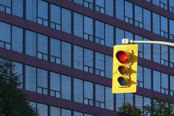 A traffic light system with the red light shining in front of a modern high-rise building with many blue windows, Toronto, Ontario, Canada, North America