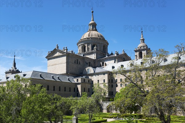 Impressive historic monastery with towers and domes surrounded by green trees under a blue sky, Real Sitio de San Lorenzo de El Escorial, Royal Seat of St Lawrence of El Escorial, palace and monastery complex, San Lorenzo de El Escorial, Madrid, Spain, UNESCO World Heritage Site, Europe