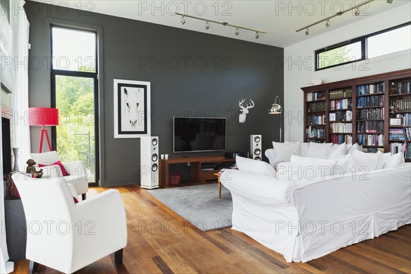 Living room with Qumaru wood floorboards, white leather armchairs, sofas, home entertainment sound system, recessed wooden wall unit, red floor lamp inside a luxurious modern cube style house, Quebec, Canada, North America