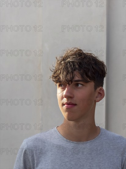 Portrait of a young athletic man with curly brown hair in front of a grey wall, looking into the distance