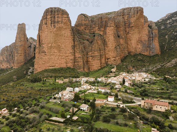 View of a small village surrounded by huge rocks and green landscape that gives a quiet and rural feeling, aerial view, Las Peñas de Riglos, As Penyas de Riglos, rock formation Mallos de Riglos, Huesca, Aragon, Spain, Europe