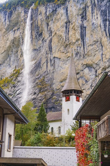 Church tower in front of a dramatic waterfall and rock face in an autumn landscape, Lauterbrunnen, Switzerland, Europe