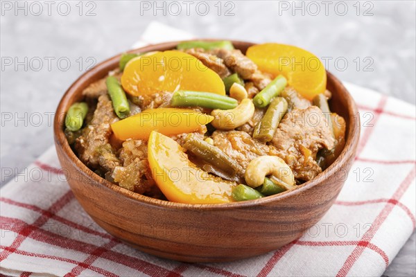 Fried pork with peaches, cashew and green beans in a wooden bowl on a gray concrete background. Side view, close up, chinese cuisine