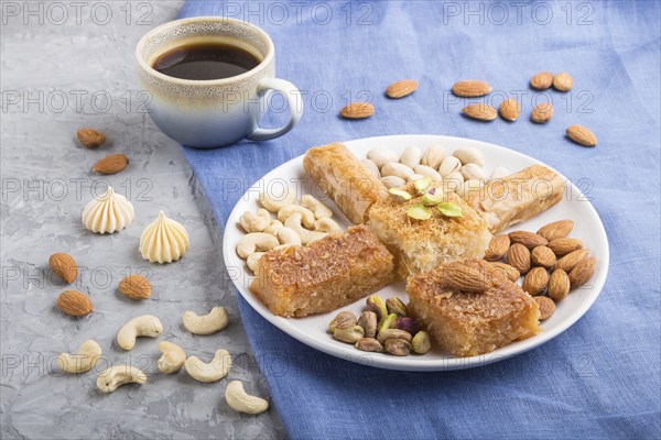 Traditional arabic sweets (basbus, kunafa, baklava), a cup of coffee and nuts on a gray concrete background and blue textile. side view, close up