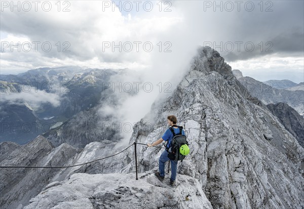 Mountaineer on a narrow rocky ridge on a steel cable, Watzmann crossing to Watzmann Mittelspitze, view of mountain panorama, Berchtesgaden National Park, Berchtesgaden Alps, Bavaria, Germany, Europe