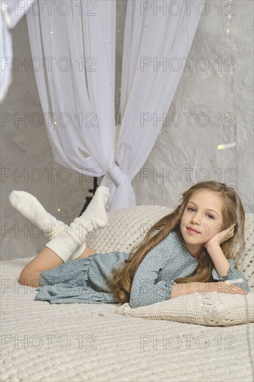 A serene image of a girl wearing a blue dress, sitting on a knitted blanket with a pillow. The soft textures and neutral tones convey a sense of comfort and tranquility