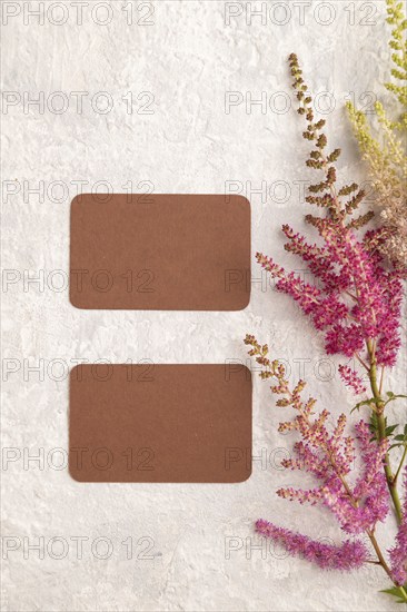 Brown paper business card mockup with purple astilbe flowers on gray concrete background. Blank, top view, copy space, still life. spring concept