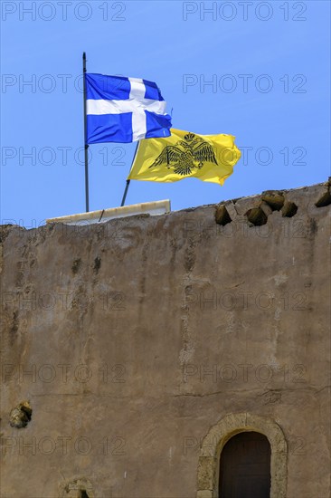 Top left flag of Crete behind it flag with symbol of Eastern Orthodox Greek Orthodox Church yellow background in black black imperial Byzantine double-headed eagle Byzantine Empire of Palaiologian Dynasty insignia of Byzantium with crown sword orb globe on monastery defence tower historic defence tower Xopatera Tower Tower of Xopateras from 19th century of Unesco Site Moni Odigitria Monastery in Festos, Crete, Crete. Unesco Site Orthodox Greek Orthodox Monastery of Moni Odigitria, Festos, Crete, Crete