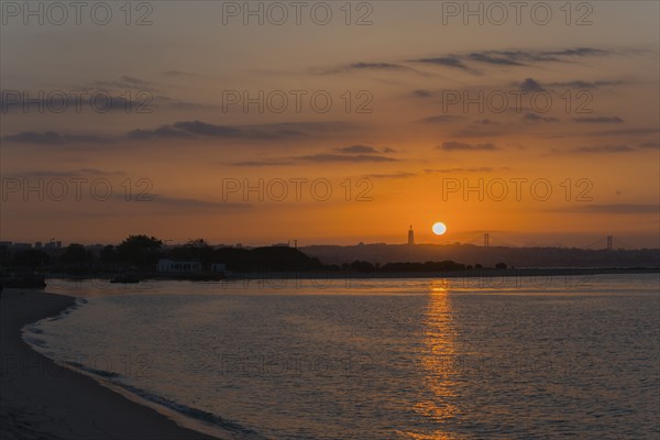 Peaceful coastal scene at sunset, the light reflects in the calm water while the sky glows in warm tones, Cristo Rei statue, Ponte 25 de Abril, 25 April Bridge, Suspension bridge over the Tagus, Lisbon, Lisboa, Portugal, Europe