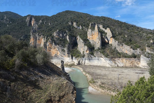 A river flows through a rocky landscape surrounded by high, steep cliffs and wooded mountains under a clear sky, Noguera Ribagorçana Mont-rebei Natural Park, Montsec mountain range, Noguera Ribagorçana river, Lleida province, Catalonia, Aragon, Spain, Europe