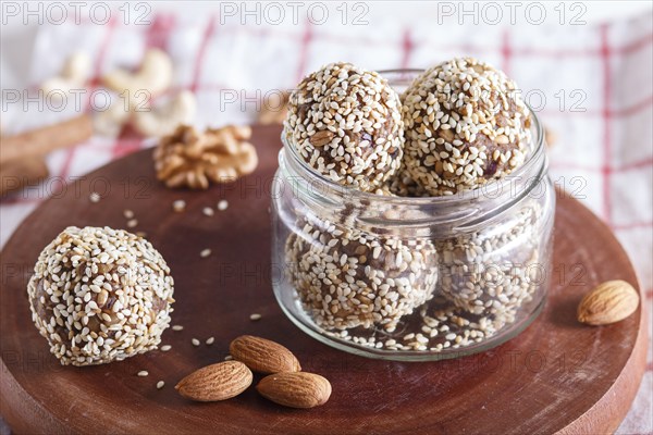 Energy balls cakes with almonds, sesame, cashew, walnuts, dates and germinated wheat on wooden board in glass jar, side view, close up