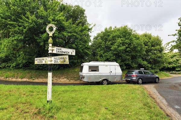 Old moss-covered signposts in the countryside, showing direction and distance to Ham, Sandwich and Deal, car with lifting roof caravan, cult, retro, rainy weather, Northbourne, Kent, Dover, England, Great Britain