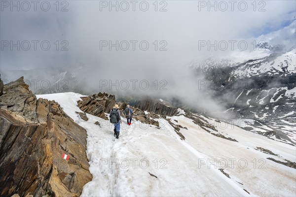 Mountaineer on a rocky ridge with snow, descent from the summit of Schönbichler Horn, view of snow-covered mountain peaks and valley Zemmgrund, Berliner Höhenweg, Zillertal Alps, Tyrol, Austria, Europe