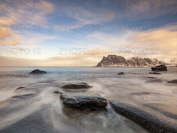 Smoothly polished rocks on Utakleiv beach in a dramatic cloudy atmosphere, snow-capped mountains in the background, Vestvagoy Island, Lofoten, Norway, Europe