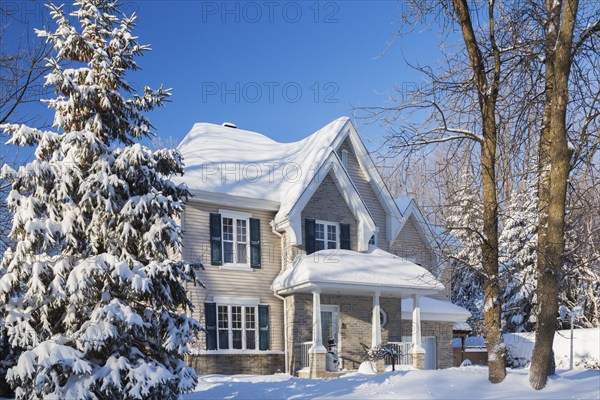 Country tan brick and vinyl cladded cottage style house facade with blue trim in winter, Quebec, Canada, North America