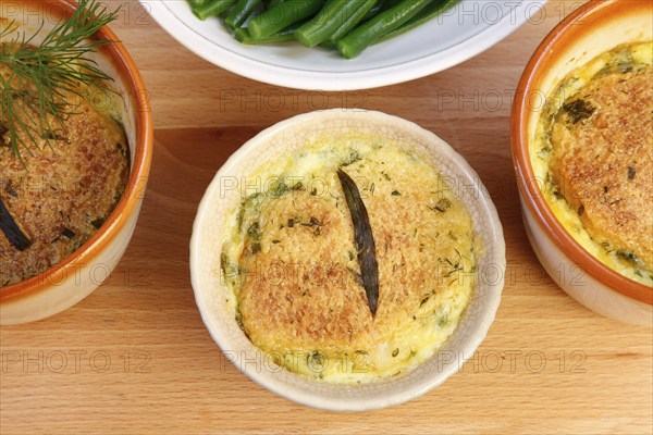 Swabian cuisine, oven-baked pike-perch with princess beans and lemon sauce, fish dish, pike-perch fillet, green beans, dill, starter, from the oven, ramekins, soufflé moulds, served on a wooden board, traditional cuisine reinterpreted, food photography, studio, Germany, Europe