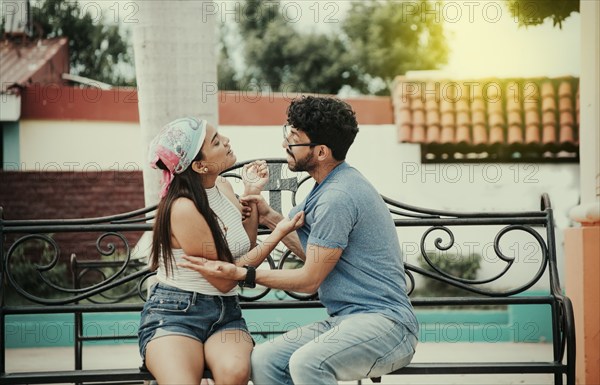 Man arguing with girlfriend sitting in a park. Young couple arguing sitting on a park bench, Concept of aggressive couples in the park. Upset couple arguing on a park bench